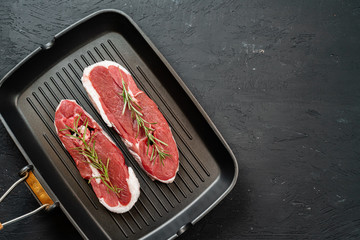 Raw steak on frying grill pan. Dark background. Close up