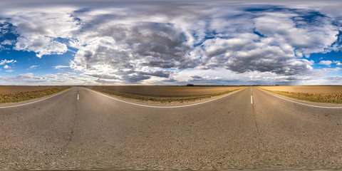 Fototapeta na wymiar Full spherical seamless panorama 360 degrees angle view on no traffic asphalt road among fields in evening before sunset with cloudy sky. 360 panorama in equirectangular projection, VR AR content