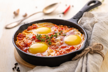 Shakshuka. Fried eggs with tomatoes and sweet pepper and herbs in a serving cast-iron frying pan.