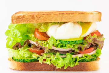 Sandwich with fresh lettuce, ham, cucumber, tomato and poached eggs isolated on white background.