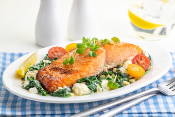 Roasted salmon fillet with spinach and cheese garnish with cherry tomatoes and lemon.