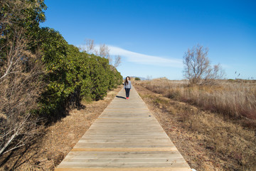 Fototapeta na wymiar Woman walking on long wooden boardwalk trail