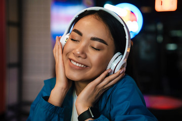 Photo of asian woman using wireless headphones and smiling in cafe