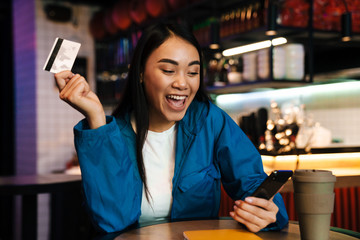 Photo of asian woman using mobile phone and holding credit card in cafe