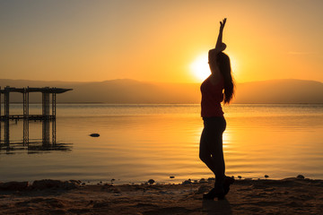 Fototapeta premium Silhouette of a young happy girl on a sunrise background near the sea. Dead sea, Israel.