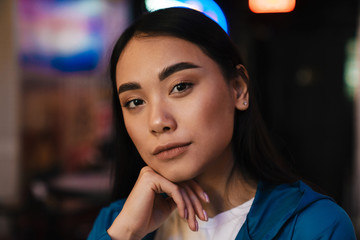 Photo of serious young asian woman looking at camera while posing