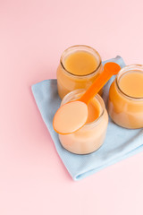 Glass jars of baby food with spoon and blue napkin on pink background
