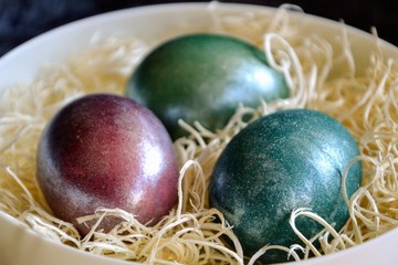 Colourful shiny easter eggs in the bowl with hay. Basket with three painted Easter eggs.Selective focus