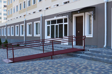 Wheelchair access ramp for entrance of residential multistory building, city street and tiles sidewalk