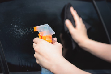 Cleaner is cleaning a car window glass with a rag and detergent close up.