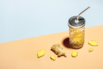 Ginger water in stylish jar with metal straw on geometric paper background and ginger slices,...