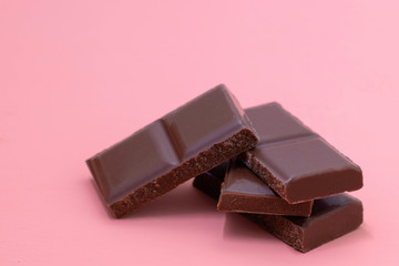 Pieces of milk chocolate on a pink background. Broken chocolate bar