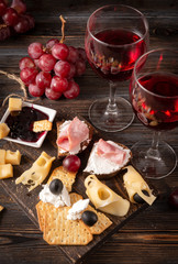 glasses of  wine , appetizer, tapas, slices of cheese, cracker, ham, jam, grapes, olives, on a dark wooden background,  top view
