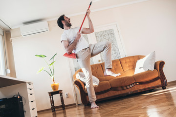 Handsome man cleaning his house with broomstick and singing and feel happy