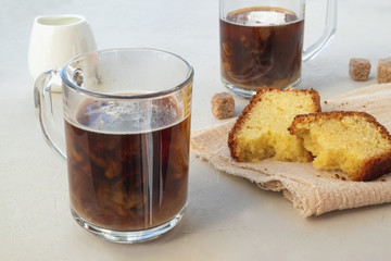 Close-up glass cup with coffee with milk and cupcake on a linen napkin on a light surface. Horizontal orientation, selective focus.