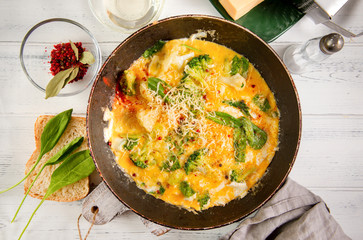 omelette with cheese, broccoli, spinach in a pan on a white wooden background,  protein Breakfast,