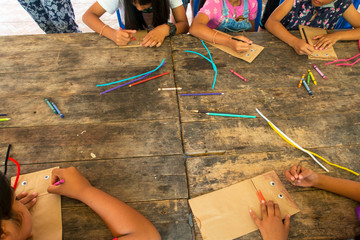 Top view of Asian kid & children group learning how to make paper puppet toy on wooden table background during free time or weaken, preschool or kindergarten daycare education concept, copy space 