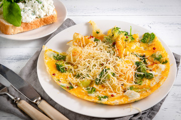 omelet with cheese, broccoli, spinach on a white plate, sandwich with cheese and greens on a white wooden , knife, fork,