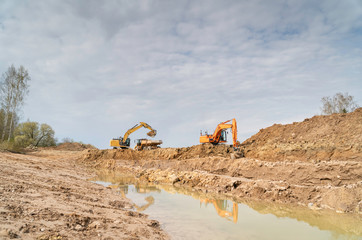 Two excavators digs out huge pond - Heavy machinery in quarry on a sunny day
