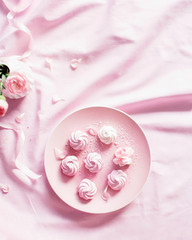 Sweet meringue on a pink plate. Roses in a white vase on a pink tablecloth. Place for the label.
