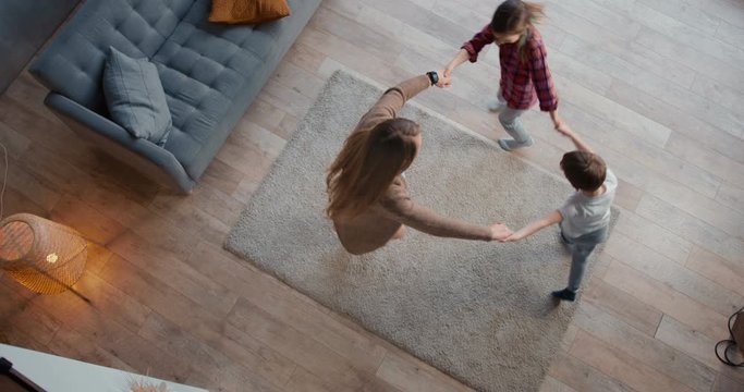Top view young happy Caucasian mother dancing round dance with two cute teen kids, going crazy on vacation at home.