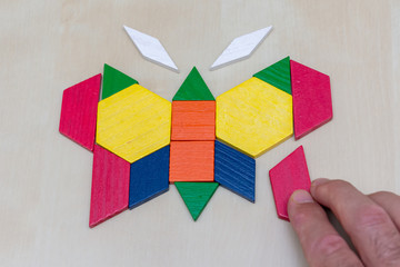 Tangram butterfly colored child geometric puzzle piece with hand filling in final piece on brown background.