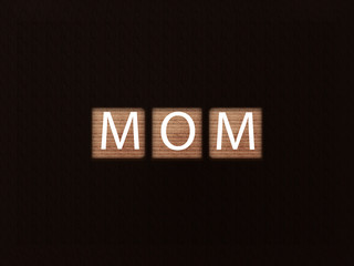The inscription MOM on wooden blocks on black background. Letter text on wooden cube.