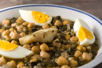 Chickpea stew with spinach and cod or potaje de vigilia on wooden table. Close up