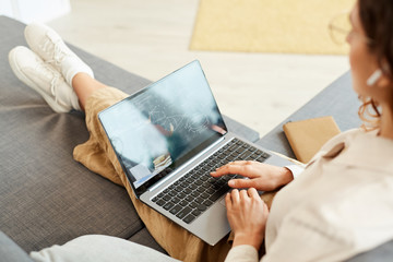Fototapeta premium Unrecognizable woman sitting on sofa at home taking part in online meeting, horizontal high angle shot