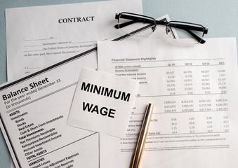 a paper with MINIMUM WAGE text on backgrounwith documents and glasses