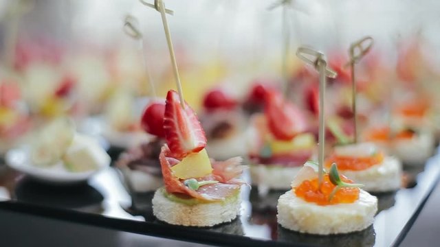 Shooting near delicious appetizers on skewers with red caviar, strawberries and slices of bacon standing on a black table tray for guests of a wedding party. Delicious appetizers perd main course.