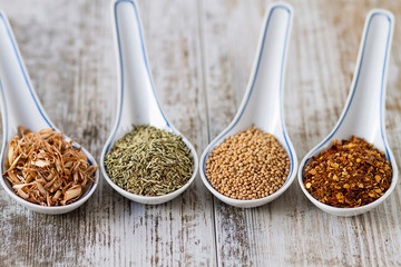 Spices and herbs in porcelain spoons over a wooden background