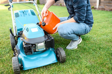 Gardening equipment in the backyard. Young guy in casual clothes refills a gas mower, the fase is...