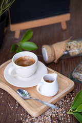 a white cub of coffee with a white cub of honey on wooden plate, background with wooden black board