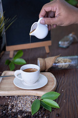 a hand holding a white honey cub drop into a white coffee cub that put on a wooden plate
