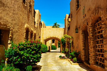 Narrow path between two old light yellow buildings with an arch under a blue sky
