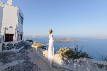 Fototapeta na wymiar Beautiful bride In a white dress posing against the background of the Mediterranean Sea in Thira, Santorini.
