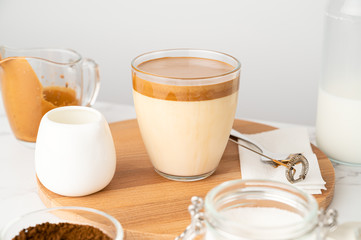 Closeup of Iced Dalgona coffee in glass cup and ingredients on light background. Trendy refreshment creamy whipped coffee. Korean coffee drink. Horizontal orientation