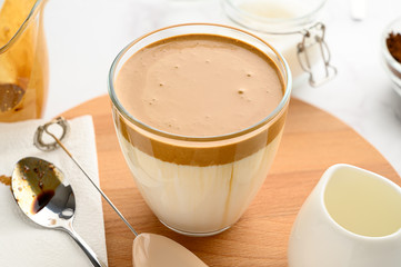 Closeup of Iced Dalgona coffee in glass cup and ingredients on light background. Trendy refreshment creamy whipped coffee. Korean coffee drink. Horizontal orientation