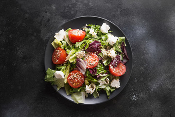 Healthy vegan salad in black dish with fresh tomato, greens, seeds hemp. Top view.