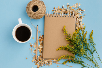 Blank brown vintage notebook, leaves, yellow flowers, pencil, cup of coffee, ball of threads on colorful blue table. Stylish minimalistic workplace concept. Top view with copy space. Flat lay - Powered by Adobe