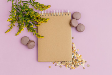 Blank brown vintage notebook, leaves, yellow flowers, pencil, diary, macaroons on purple table. Stylish minimalistic workplace concept. Top view with copy space