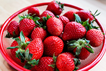 Strawberries in red bowl on wooden background.