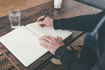 rear view of man sitting at coffee table writing in diary or notebook