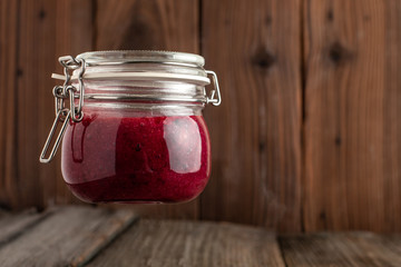 Home made vegan raw raspberry jam in a glass jar on wooden background. Healthy raw jam.