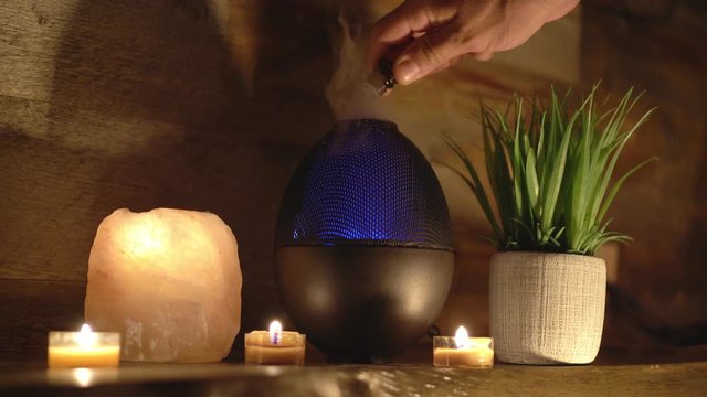 4k, Woman adding essential oil to electric diffuser lamp, candles on wooden table in room. Aromatherapy.