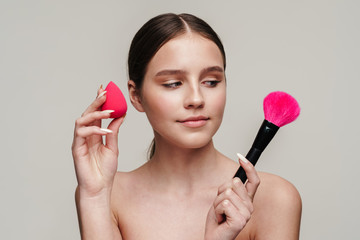 Image of beautiful young shirtless woman using makeup sponge and brush
