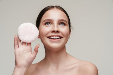 Image of pleased young shirtless woman showing makeup pad and smiling