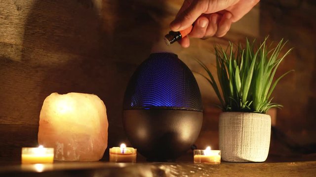 4k, Woman adding essential oil to electric diffuser lamp, candles on wooden table in room. Aromatherapy.