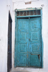 An old, broken, wooden blue door at whitewashed village house on the Greek island of Sikinos. Peeling, scuffed paint and chipped, worn woodwork.  